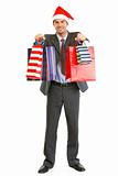 Smiling businessman in Santa hat giving shopping bags
