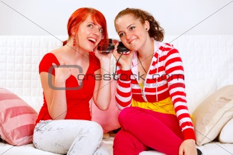 Sitting on sofa two pretty girlfriends holding headphones and listening music
