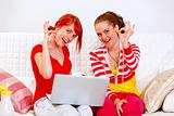 Laughing girlfriends using laptop and showing ok gesture
