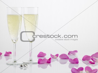 Two Wedding Rings Next To Champagne Flutes And Rose Petals