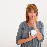 young woman holding alarm clock and hushing 