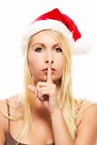 beautiful blonde woman wearing santa's hat putting finger on mouth to shhht