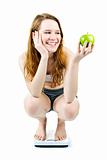Young smiling girl on bathroom scale holding apple