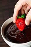 Hand dipping strawberry in chocolate