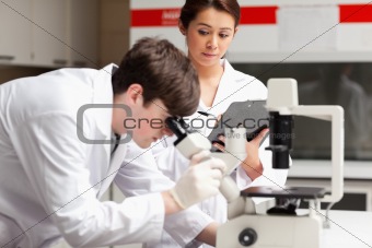 Science student looking in a microscope while his classmate is writing