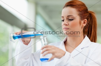Young scientist pouring blue liquid in an Erlenmeyer flask
