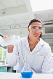 Portrait of a female science student pouring liquid with protective glasses