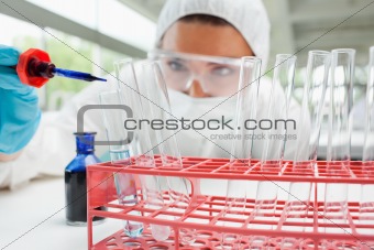 Protected female scientist dropping blue liquid in a test tube