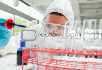 Protected female science student dropping blue liquid in a test tube