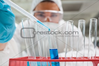 Protected science student dropping blue liquid in a test tube