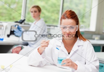 Scientist dropping liquid in a beaker while her colleague is using a microscope