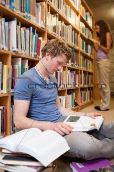 Portrait of a male student reading books while his classmate is reading