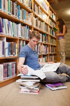 Portrait of a male student making research while his classmate is reading