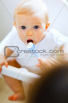Eat smeared adorable baby in baby chair feeding by mother
