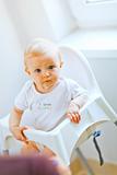 Eat smeared adorable baby in baby chair interestedly looking
