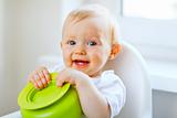 Adorable baby girl sitting in baby chair and playing with plate
