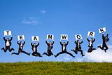 happy businessman holding teamwork text and jumping on the green field