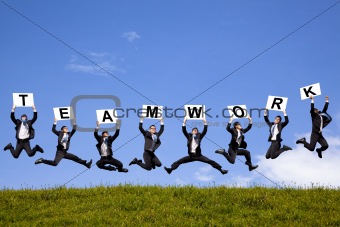 happy businessman holding teamwork text and jumping on the green field