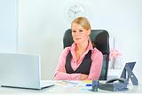 Pretty business woman sitting at office desk with crossed arms
