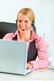 Smiling business woman with headset working on laptop
