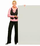 Full length portrait of smiling business woman pointing on blank board
