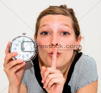 beautiful young woman holding alarm clock and hushing 