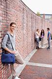 Portrait of a male student leaning on a wall while his friends are talking