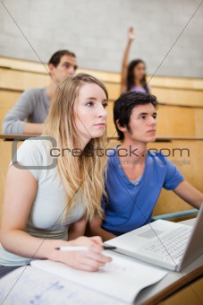 Portrait of students listening a lecturer while their classmate is raising her hand