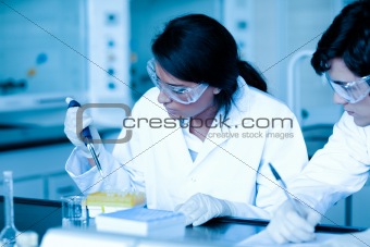 Scientist dropping liquid in test tubes while her partner is taking notes