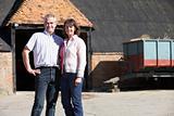 Farmer And Wife Standing In Front Of Farm Buildings