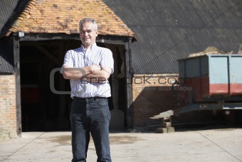 Farmer Standing In Front Of Farm Buildings
