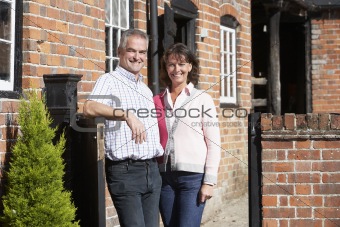 Farmer And Wife Standing In Front Of Farmhouse