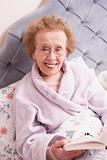 Senior Woman Relaxing In Bed With Book