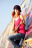Beautiful red-haired girl with guitar and graffiti wall at backg