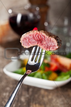 slice of a steak on a fork over salad