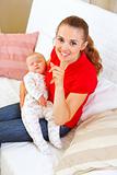 Happy mother holding sleeping baby and showing shhh gesture
