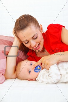 Young mother laying on couch and playing with baby 
