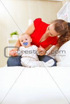 Young mother laying on couch and playing with baby 
