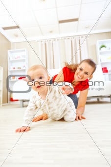 Smiling mommy playing with creeping on floor baby
