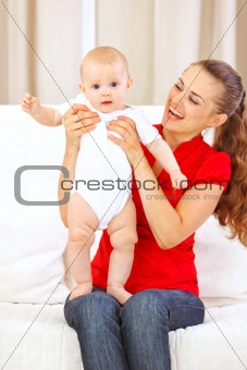Happy mothers helping little baby standing on her laps
