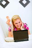 Smiling young woman lying on sofa and using laptop
