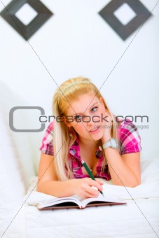 Pensive young woman lying on sofa with notebook and pen
