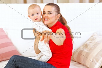 Happy mother sitting on divan and showing something to her baby
