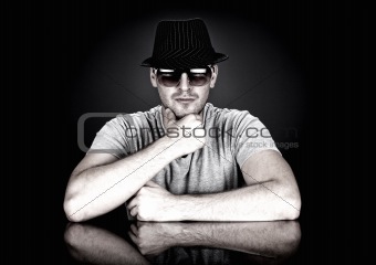 man in hat and sunglasses sitting behind desk looking at camera
