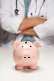 Female Doctor with Folded Arms Behind Piggy Bank Abstract.
