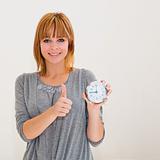 beautiful young woman holding alarm clock with thumbs up 