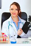 Portrait of female medical doctor sitting in cabinet with clipboard
