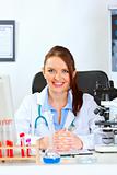 Smiling female medical doctor sitting at table in her cabinet 

