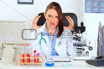 Stressed female medical doctor sitting at office table and holding hands near head
