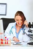 Smiling female medical doctor talking on phone and looking in clipboard

